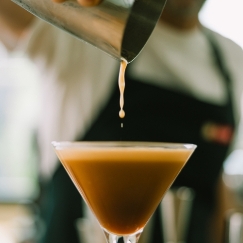 Barista Malongo versant un filet d'espresso/vodka frais dans un verre à martini pour réaliser un Espresso Martini , avec mousse caramelisée caractéristique